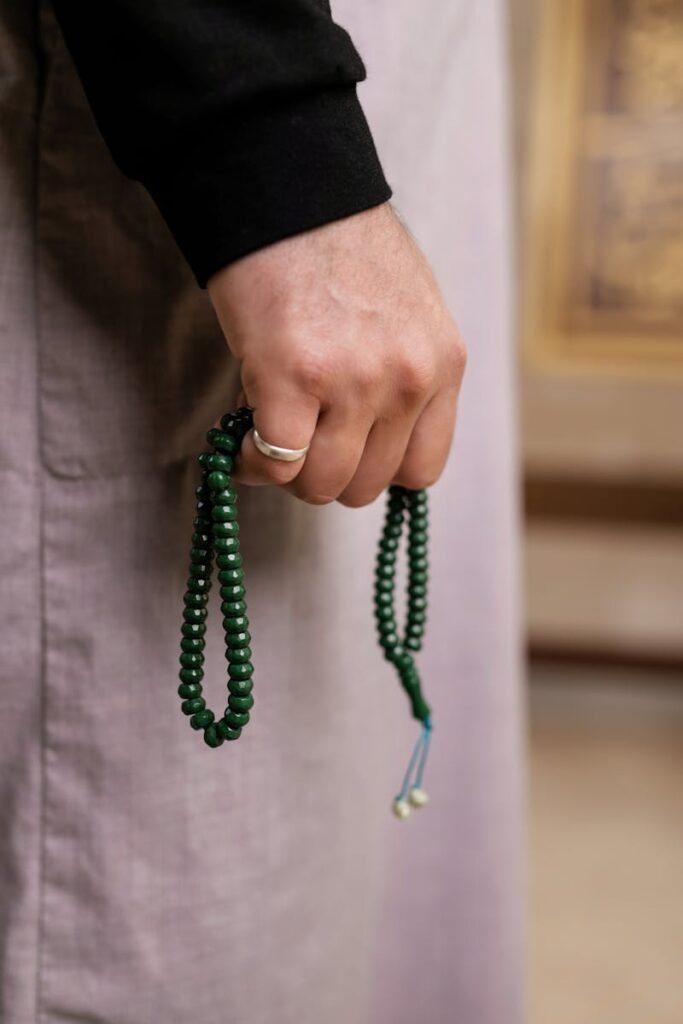 About A close-up image of a hand holding green prayer beads, symbolizing meditation or spirituality.